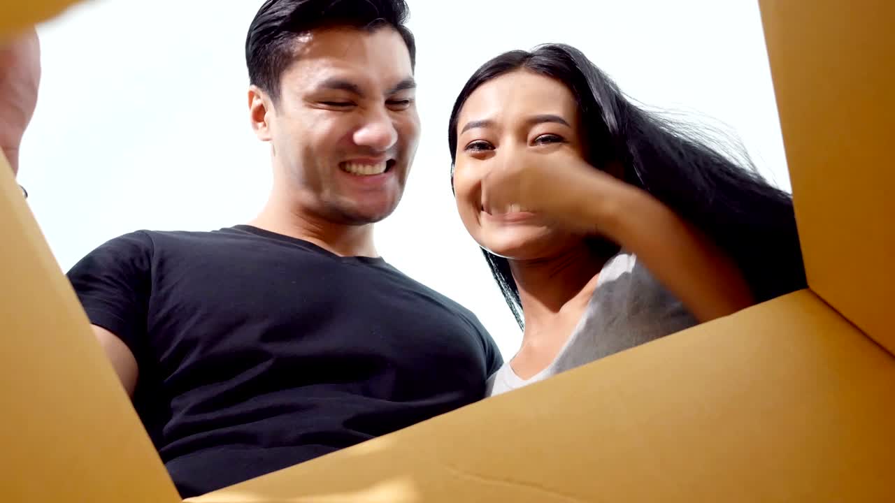 남자와 여자는 집에서 함께 행복한 감정으로 상자를 열고, 남자는 아내를 놀라게 하고, 집에서 그녀에게 선물을 선물합니다.