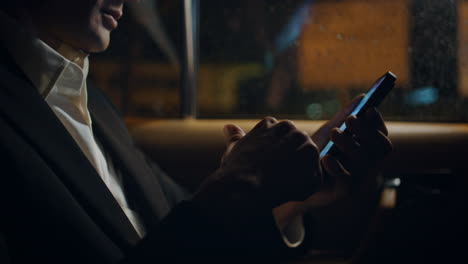 hombre de negocios de primer plano con la mano desplazando el teléfono celular en el coche de la noche. jefe con el móvil
