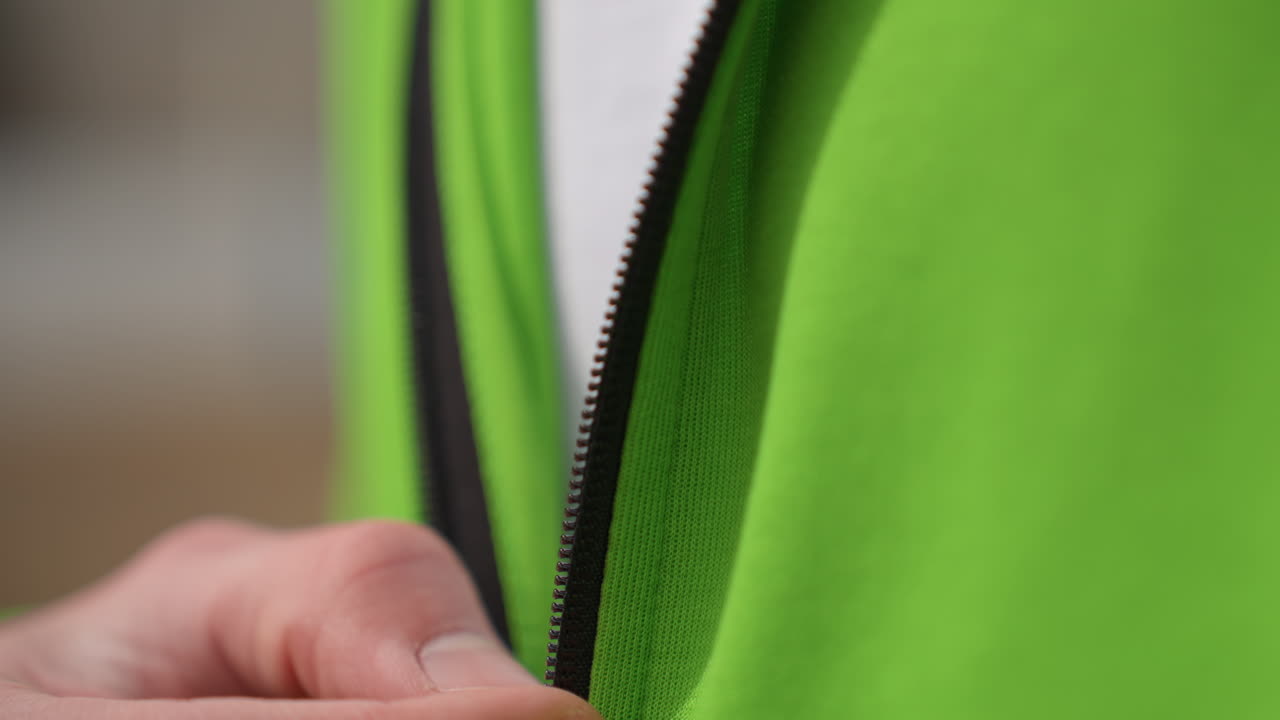 Preparándose para actividades al aire libre con chaqueta con cremallera; dedos subiendo la cremallera de la chaqueta durante el entrenamiento al aire libre; primer plano de las manos subiendo la cremallera de la chaqueta verde durante la preparación para el entrenamiento al aire libre