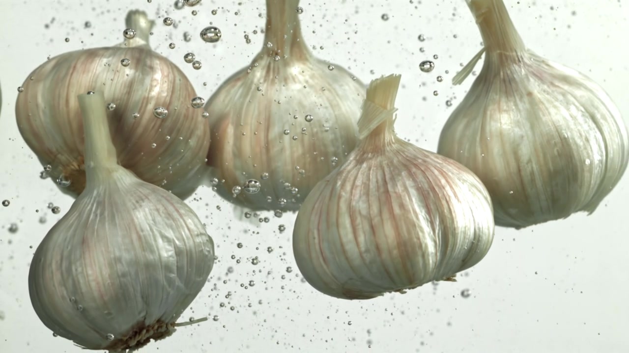 Bulbi d'aglio freschi galleggianti nell'acqua con bolle d'aria