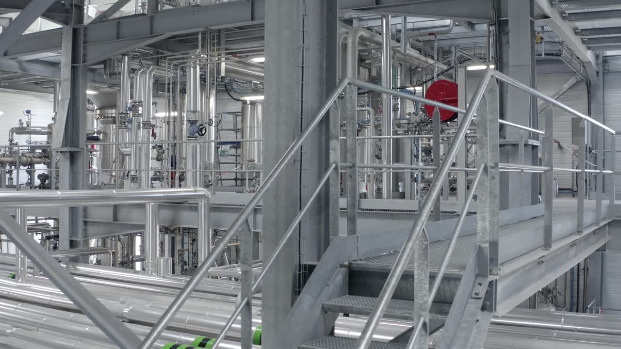 Inside manufacturing plant showing complex network of metal pipes, platforms, and stairs, industrial engineering, Castets, France