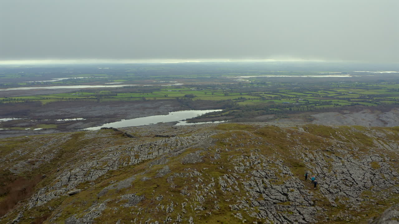Dynamic aerial shot flying over Mullaghmore Peak, showcasing hikers and stunning Burren views