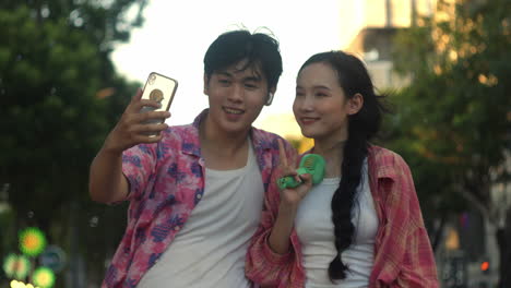 asiatic-couple-of-lovers-taking-a-selfie-with-smartphone-while-making-soap-bubble-outdoor-in-main-square-during-summer-holiday-vacation-trip