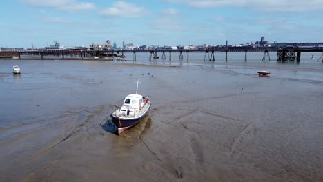 Small-sailing-boat-stranded-in-low-tide-muddy-marshland-coastline-aerial-view-orbit-low-right