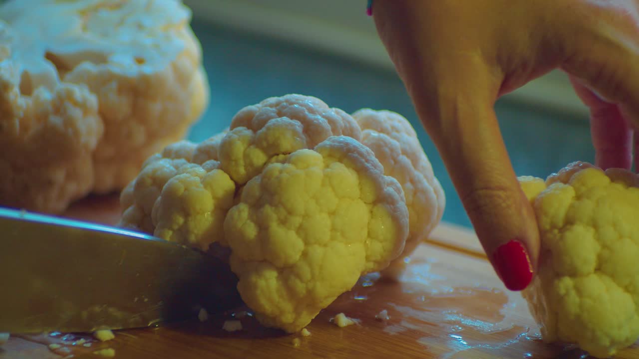 cortar la coliflor blanca fresca en la mesa de la cocina con un cuchillo como preparación para la comida