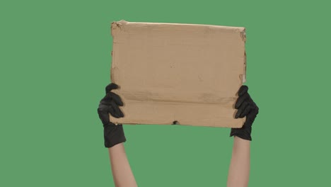 manos con guantes negros levantan un cartel en blanco hecho de una caja de cartón. espacio vacío para su texto, logotipo o anuncio. concepto de diseño de banner. aislado una pantalla verde, clave de croma. cerrar. cámara lenta