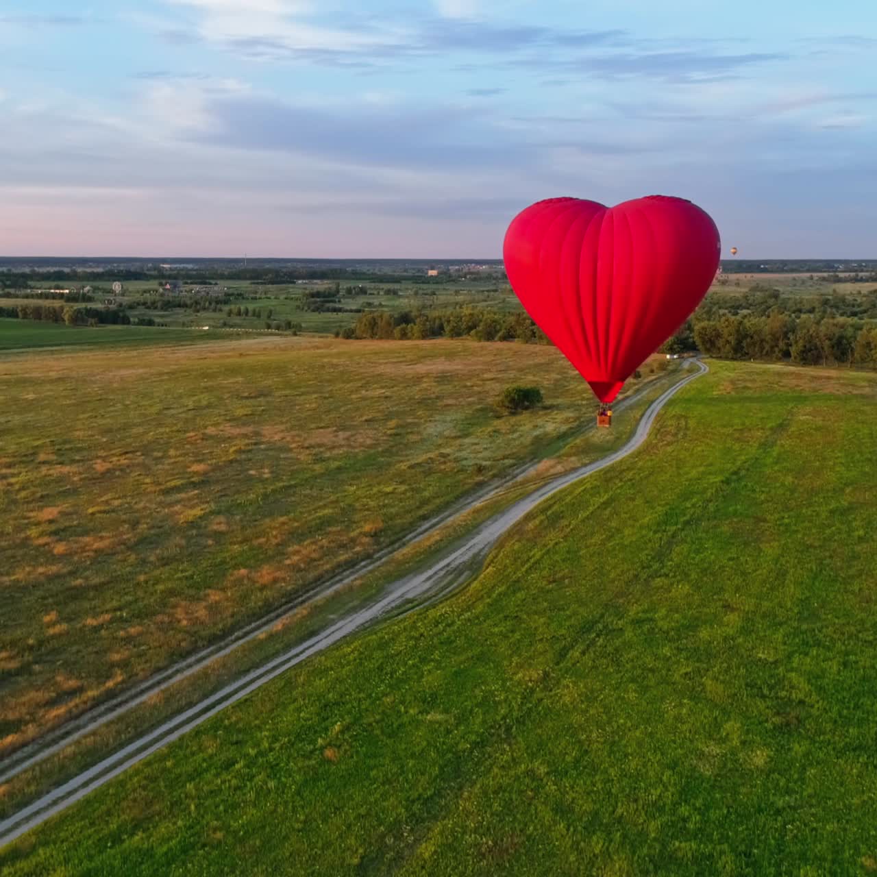 Travel of romantic hot air balloon. Red aerostat balloon flying over the fields under blue sky. Beautiful aerostat in the form of a heart.Aerial view.