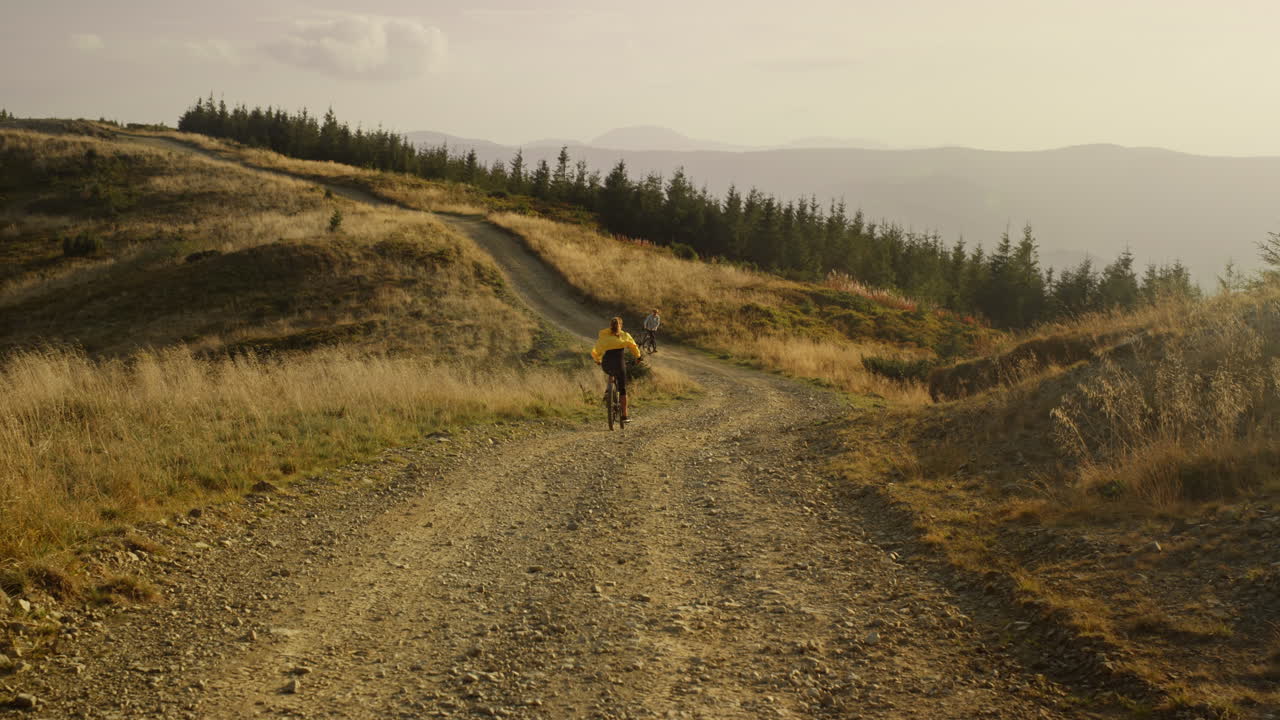 Woman on bike riding down mountain road. Couple of bicyclists training together