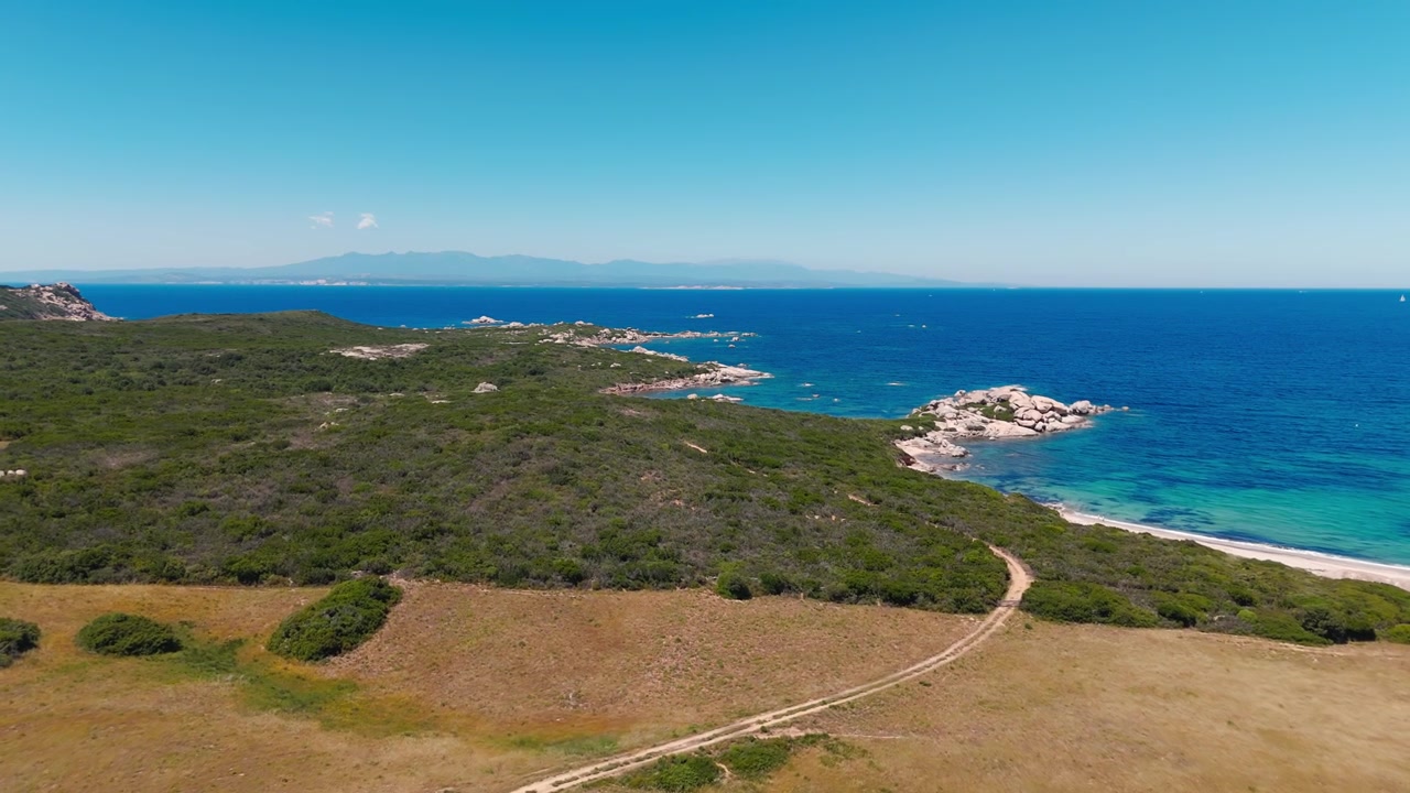 Vista aerea di un paesaggio costiero con sentiero sinuoso, colline verdi e mare blu