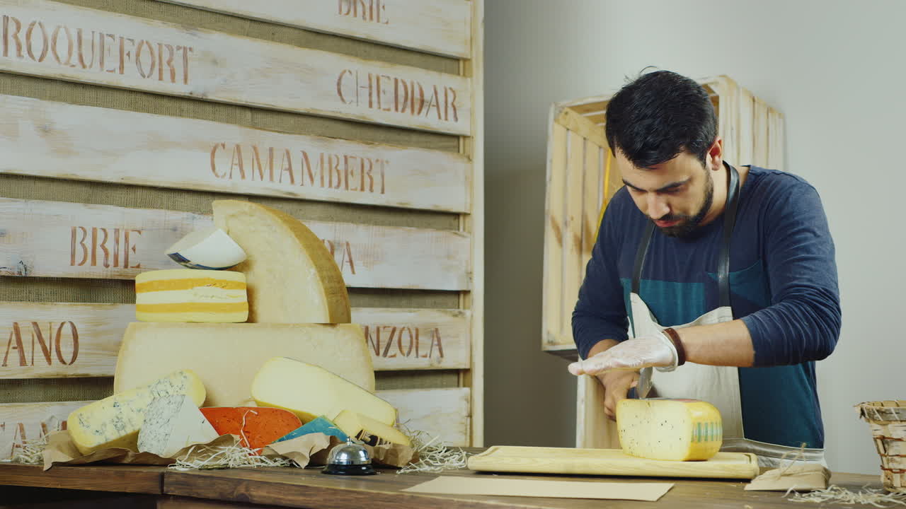 hombre atractivo que trabaja en la tienda de queso en lonchas de queso y luego lo envuelve en un sobre de papel