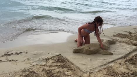 little girl on vacation plays on beach building sand dolphin on seashore