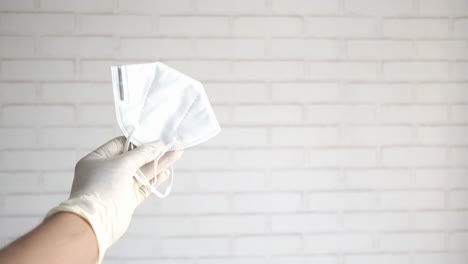 hand in glove holding a white face mask