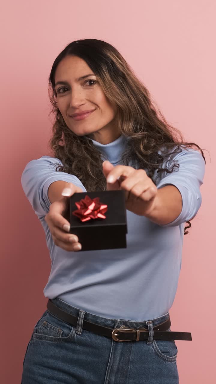 Smiling adult woman giving a gift box looking at camera. Vertical footage