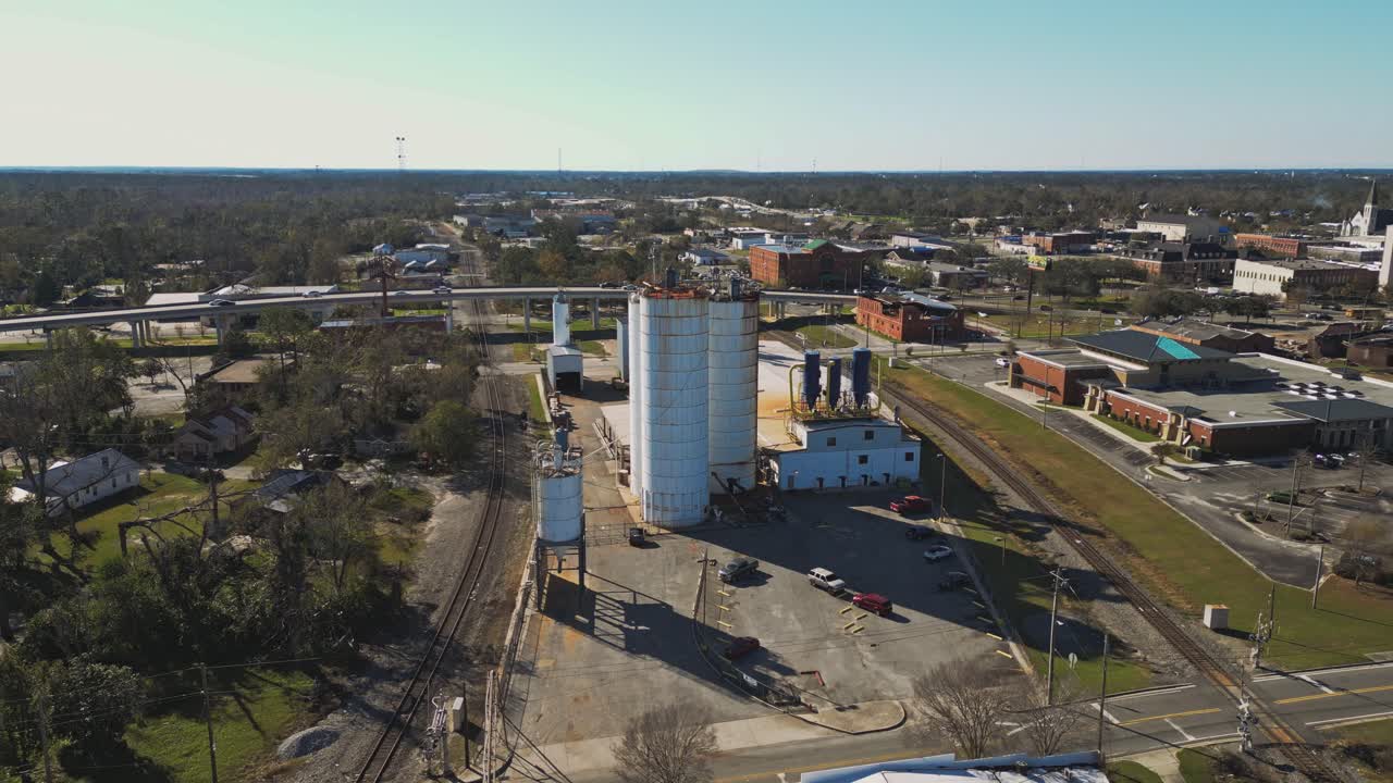 An Industrial Facility With Large Storage Silos Stands Near Railroad Tracks in a Small City - Aerial Drone Shot