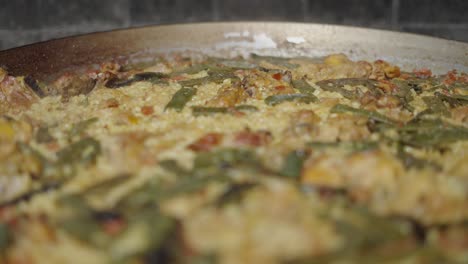 a close-up of a traditional paella-like rice and chicken dish with green beans cooking in a large pan