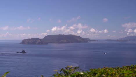 View-out-on-beautiful-blue-ocean-with-clouds-in-distance,-pants-in-foreground-and-boat-passing-through