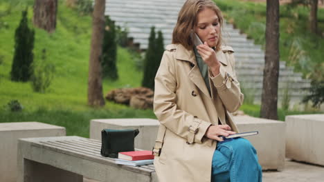 caucasian female student with smartphone and books at the park.