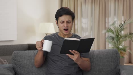 Tired-Indian-man-reading-a-book-and-drinking-coffee