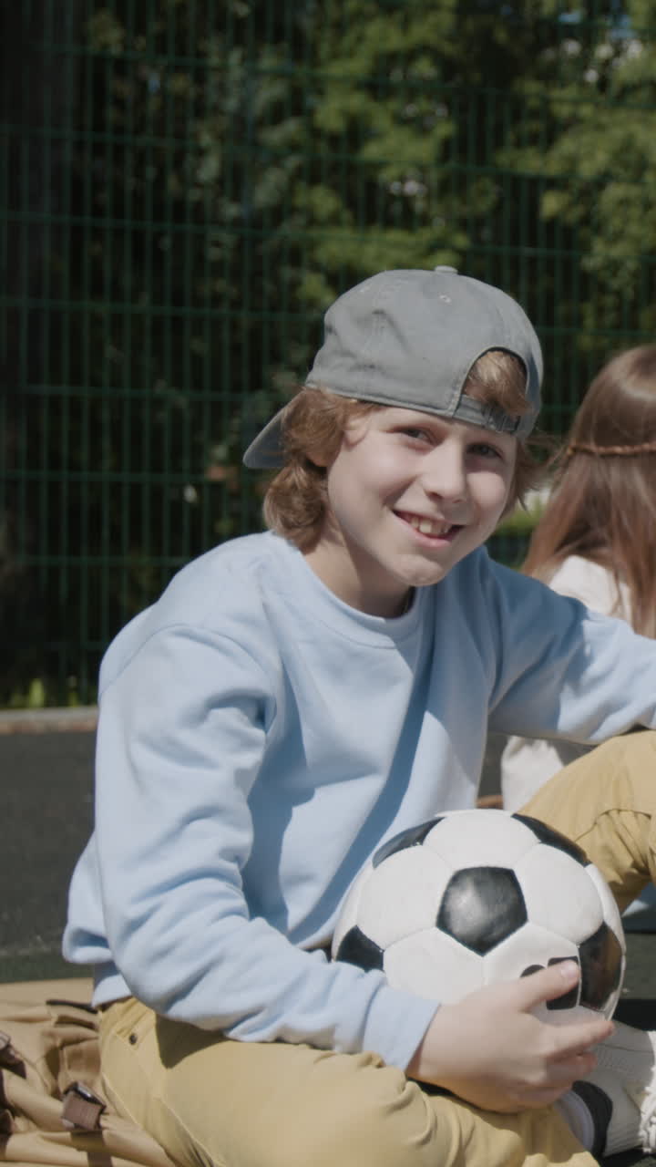 Young boy adjusting his cap with a soccer ball nearby