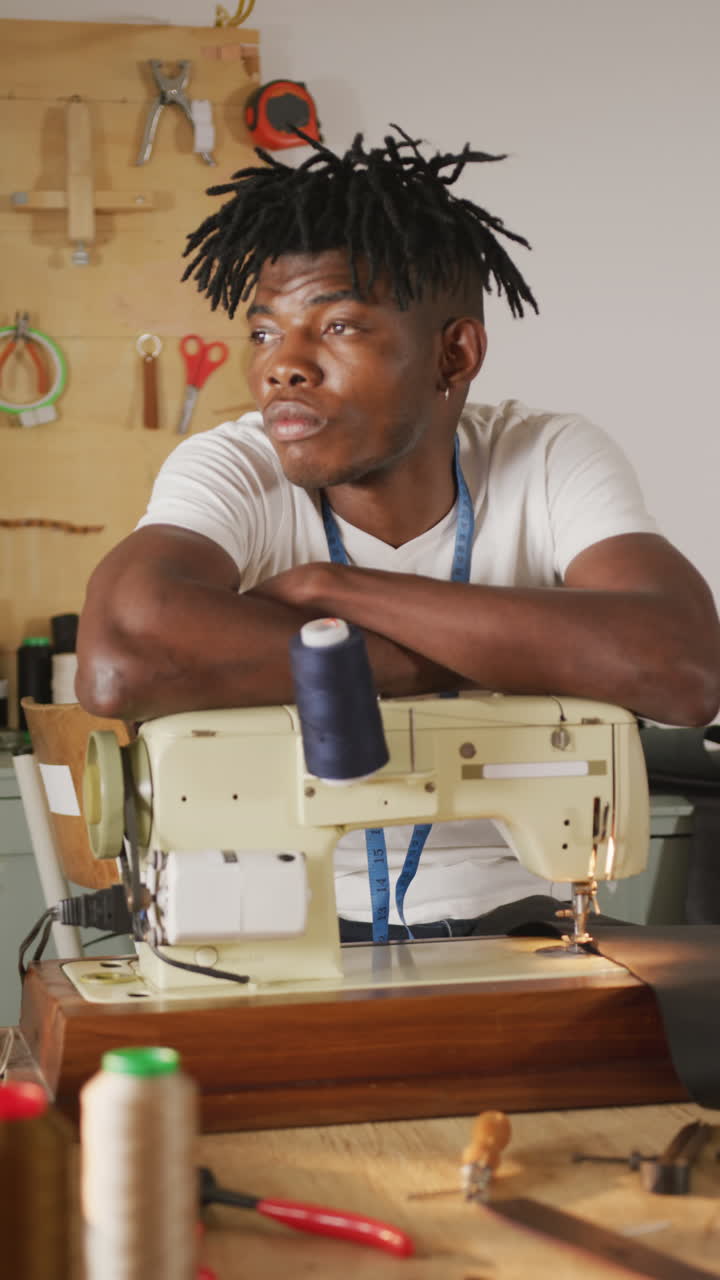 Video verticale di un artigiano del cuoio afroamericano con i dreadlock alla macchina da cucire in laboratorio