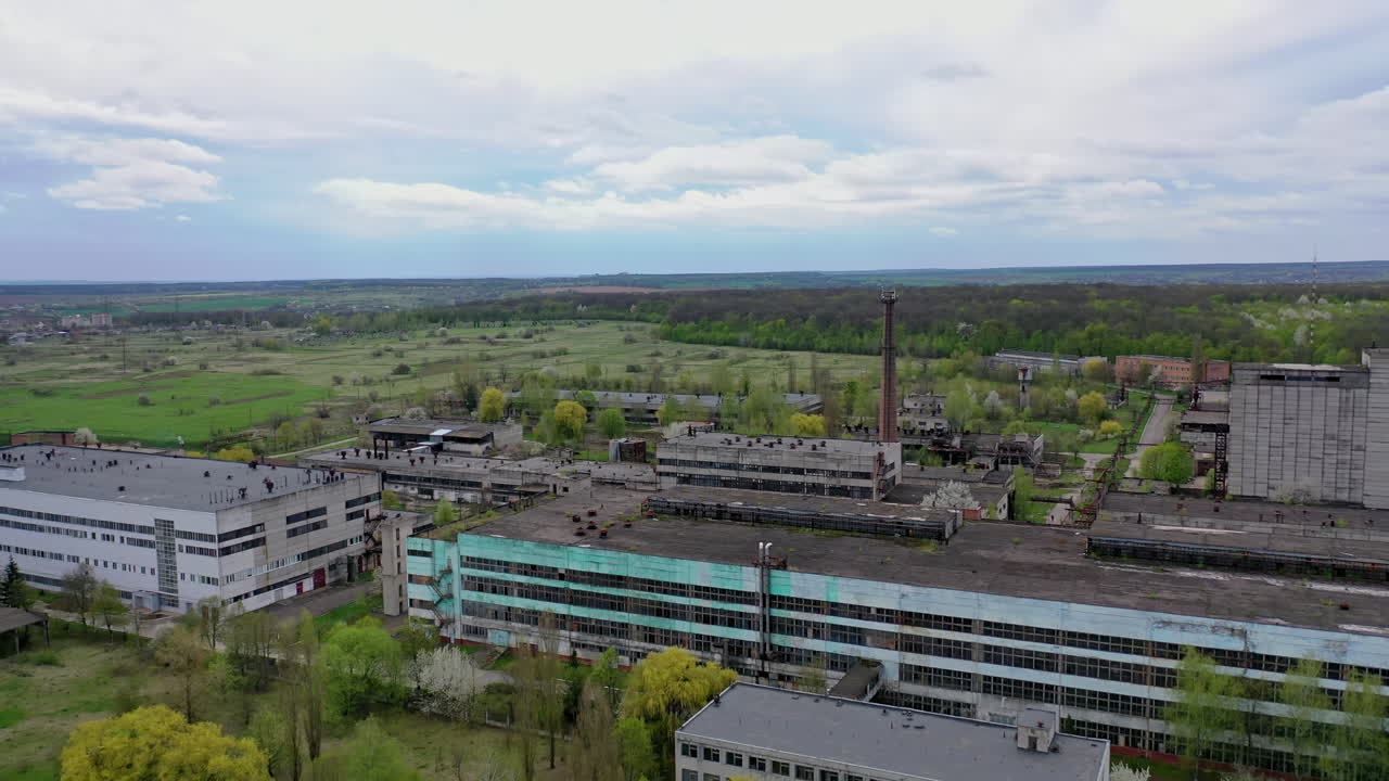 Large factory among beautiful green nature. Exterior of industrial plant in the countryside. Old architectural buildings of a manufacturing.