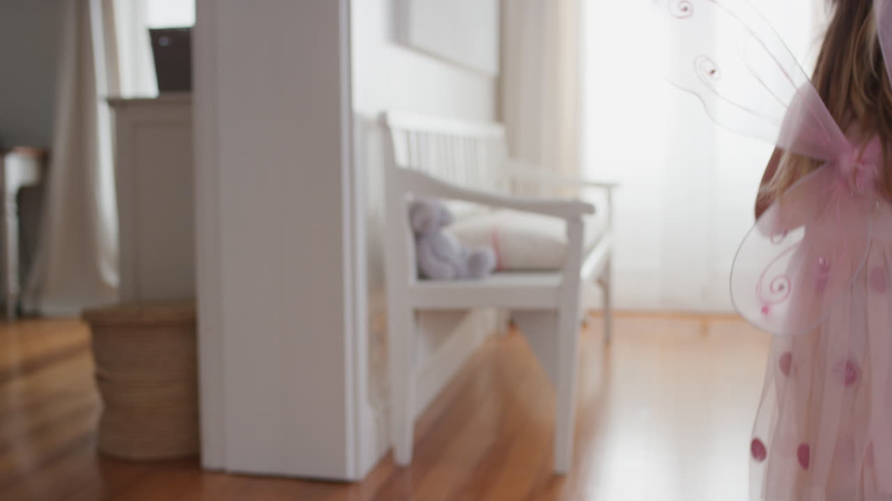 очаровательная маленькая девочка в милых крыльях держит плюшевого медведя игрушку играет одеваться счастливый ребенок весело смотрит в окно в доме 4k