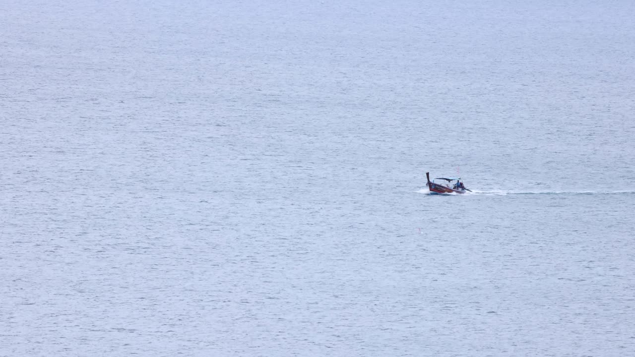 태국 푸켓의 평온한 바다를 가로질러 날아다니는 롱테일 보트, 부드러운 조명과 함께 조용하고 넓은 각도 프레임으로 포착되었습니다.