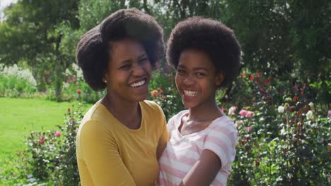 portrait of smiling african american mother and daughter embracing in sunny garden