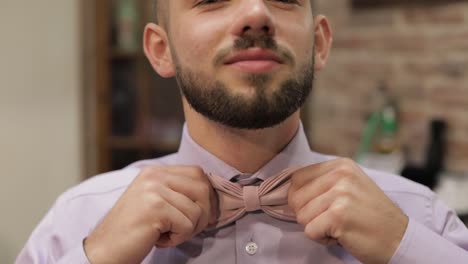 Groom-adjusts-bow-tie-in-barbershop-background.-Preparing-to-go-to-the-bride