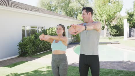 feliz pareja caucásica haciendo yoga y estirándose en un jardín soleado, cámara lenta