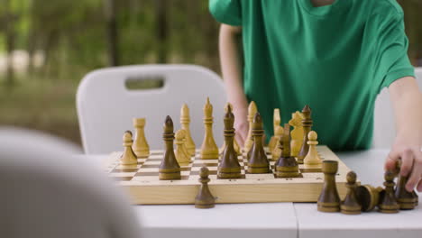 kleiner junge, der auf dem campingplatz im wald ein schachbrett aufstellt