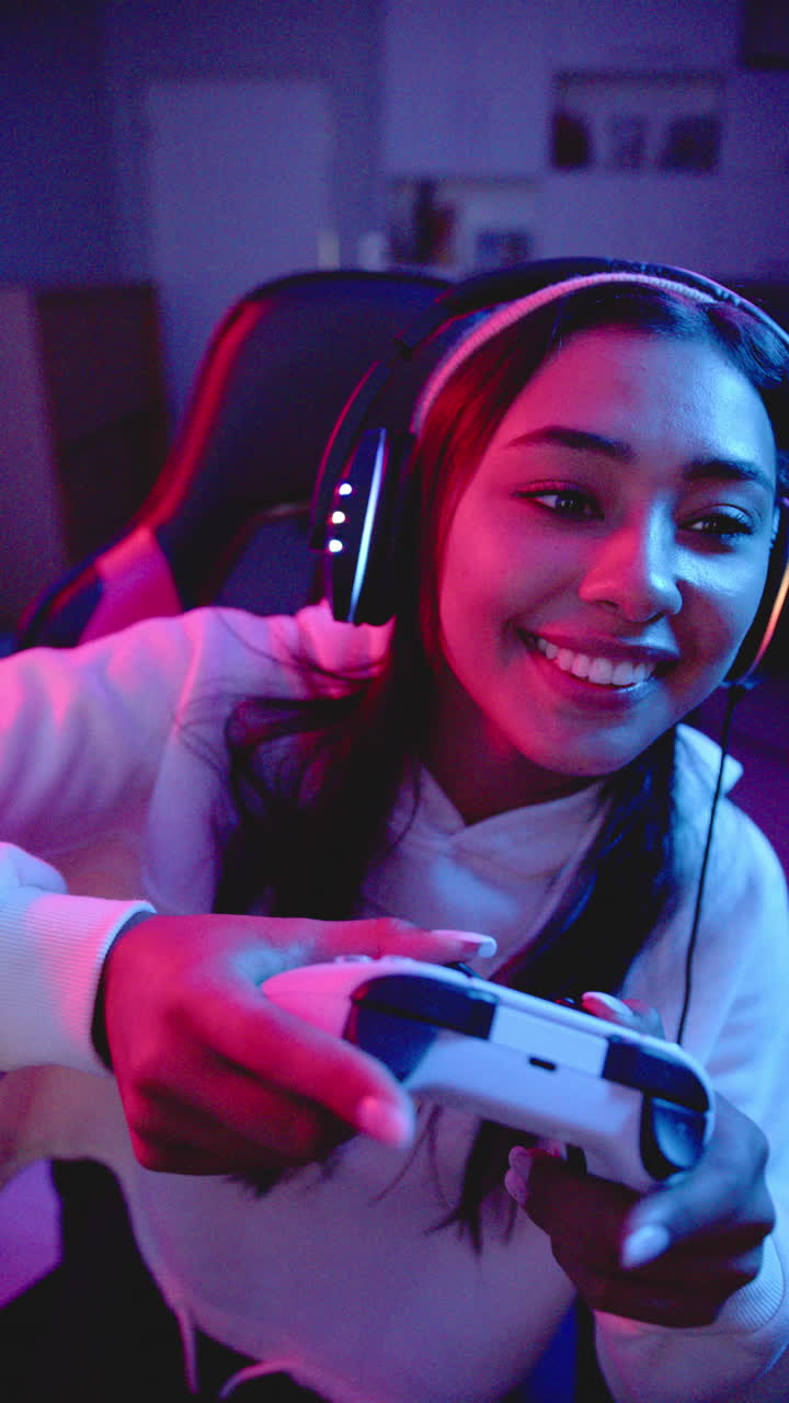 Video verticale: Donna che gioca ai videogiochi, con le cuffie e sorridente su una sedia da gaming.