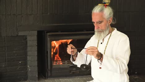 elderly spiritual practitioner with tingsha against fireplace