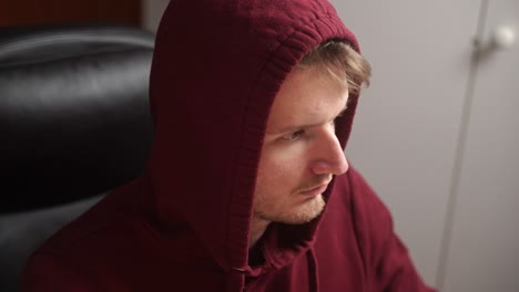 a young man with a college hoodie on sits down in a home office chair and proceeds to execute some code on a computer