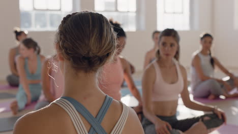 instructor de clase de yoga enseñando ejercicios de estiramiento del cuello a un grupo saludable de mujeres que disfrutan practicando posturas en el gimnasio al amanecer.