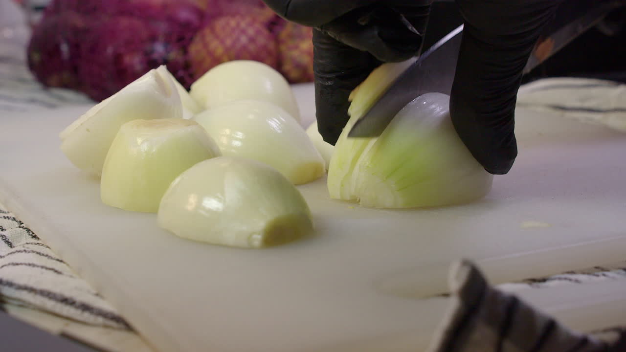 Close up gloved chef hands slice raw white onion on cutting board