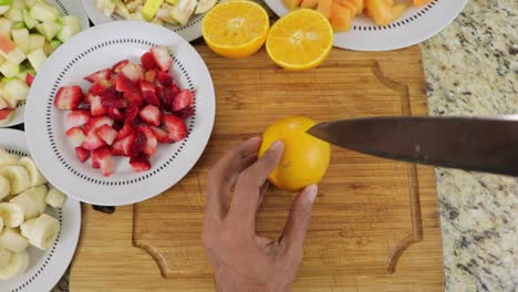 top view of male hands cutting oranges into equal halves on cutting board