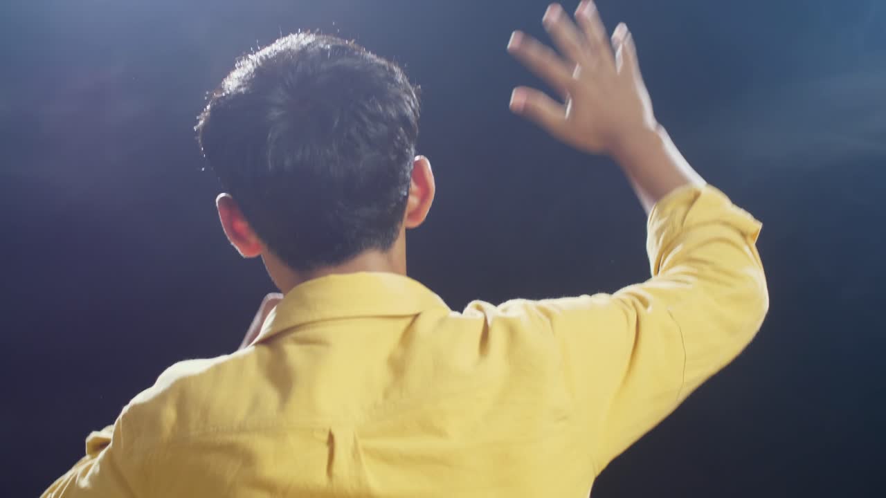 젊은 아시아 소년이 마이크를 들고 색 연기와 검은색 배경에 을 치는 가까운 뒤의 모습