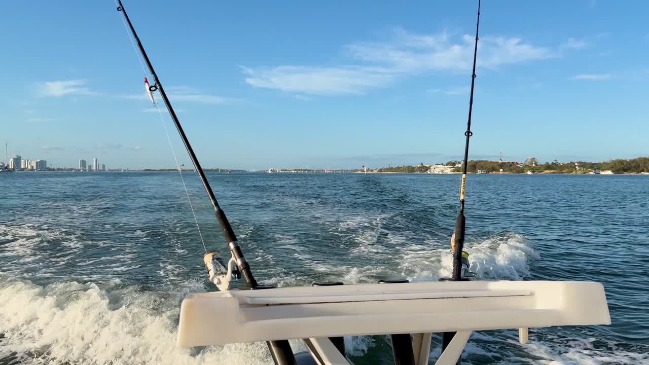 Rear view of fishing rods on moving boat, city skyline, blue sky, bright natural lighting