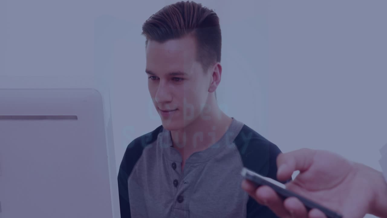 Uomo seduto che lavora alla scrivania, una mano porta uno smartphone e attiva un HUD che mostra un avviso di cyber sicurezza