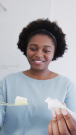 vertical video of portrait of african american woman brushing her teeth on light background
