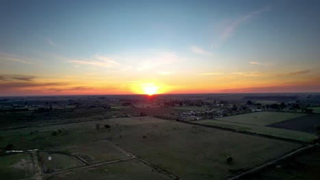 Puesta-De-Sol-Campestre-En-Los-Campos-Y-El-Pueblo,-Zoom-Panorámico-De-Drones-Aéreos