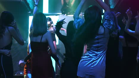 group of people dance in disco night club to the beat of music from dj on stage