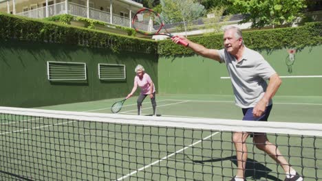 happy caucasian senior couple playing as a doubles team at outdoor tennis court after playing a game