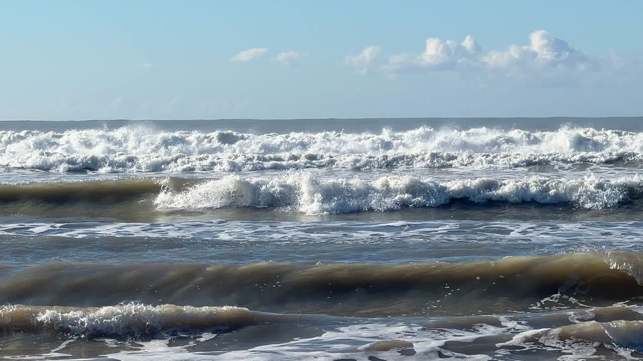 Inquadratura fissa di forti onde atlantiche che si infrangono di giorno sotto un cielo blu vicino alla costa di Barbate, nel sud della Spagna.
