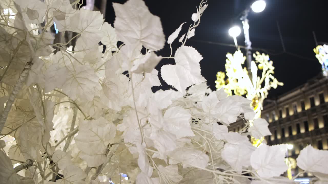 Person touching white leaf decorations in a city at night