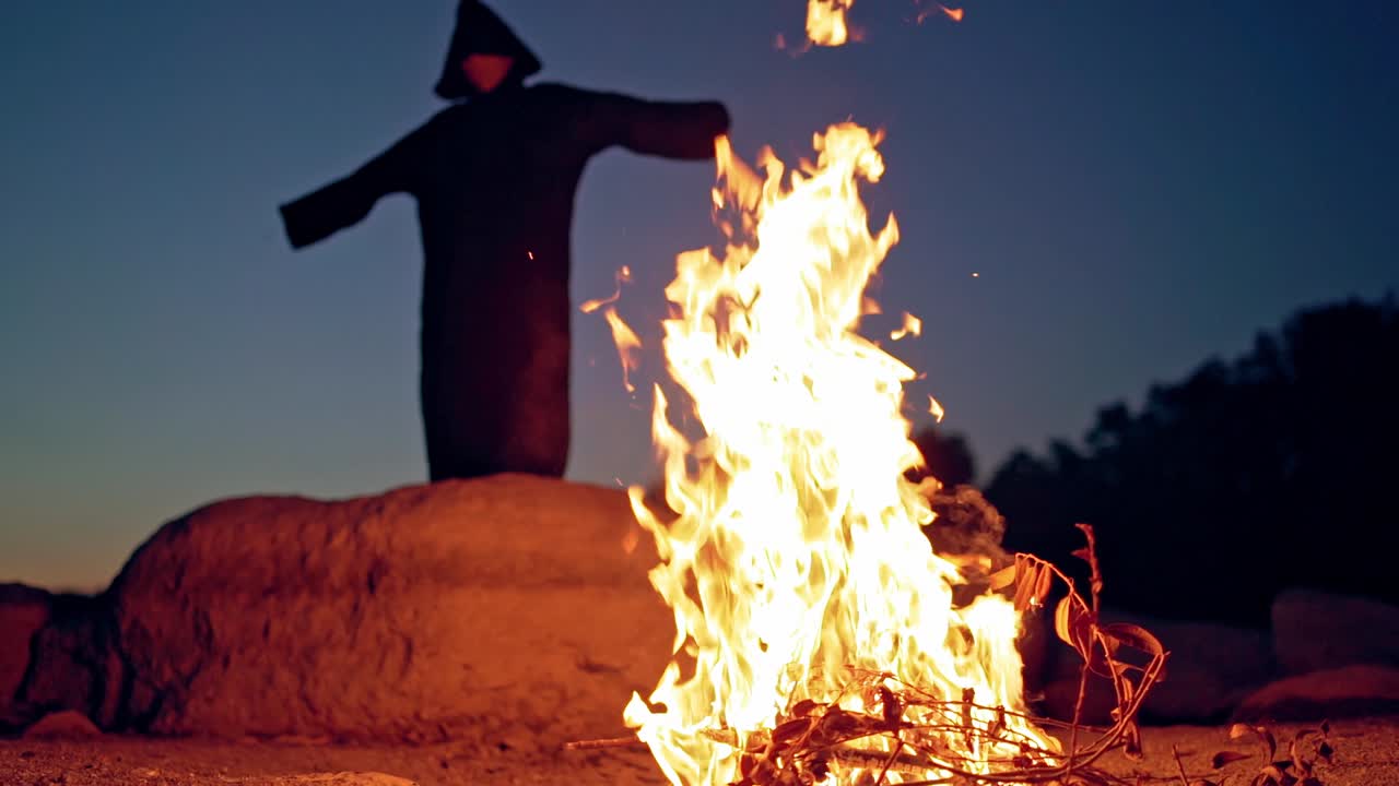 Scary figure in black mantle. Close up of witch stay around the fire in forest