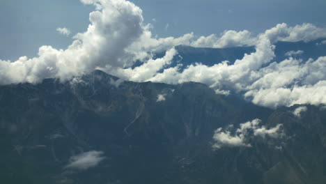 White-clouds-over-mountain-above-airplane-flying-in-blue-sky.