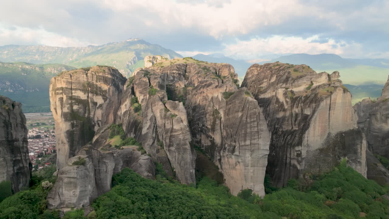 ฟุตเทจทางอากาศที่สวยงามของกลุ่มหินและอาราม Meteora ในกรีซ พร้อมทิวทัศน์สีเขียวชอุ่มและหน้าผาที่สวยงามภายใต้ท้องฟ้าที่มีเมฆ
