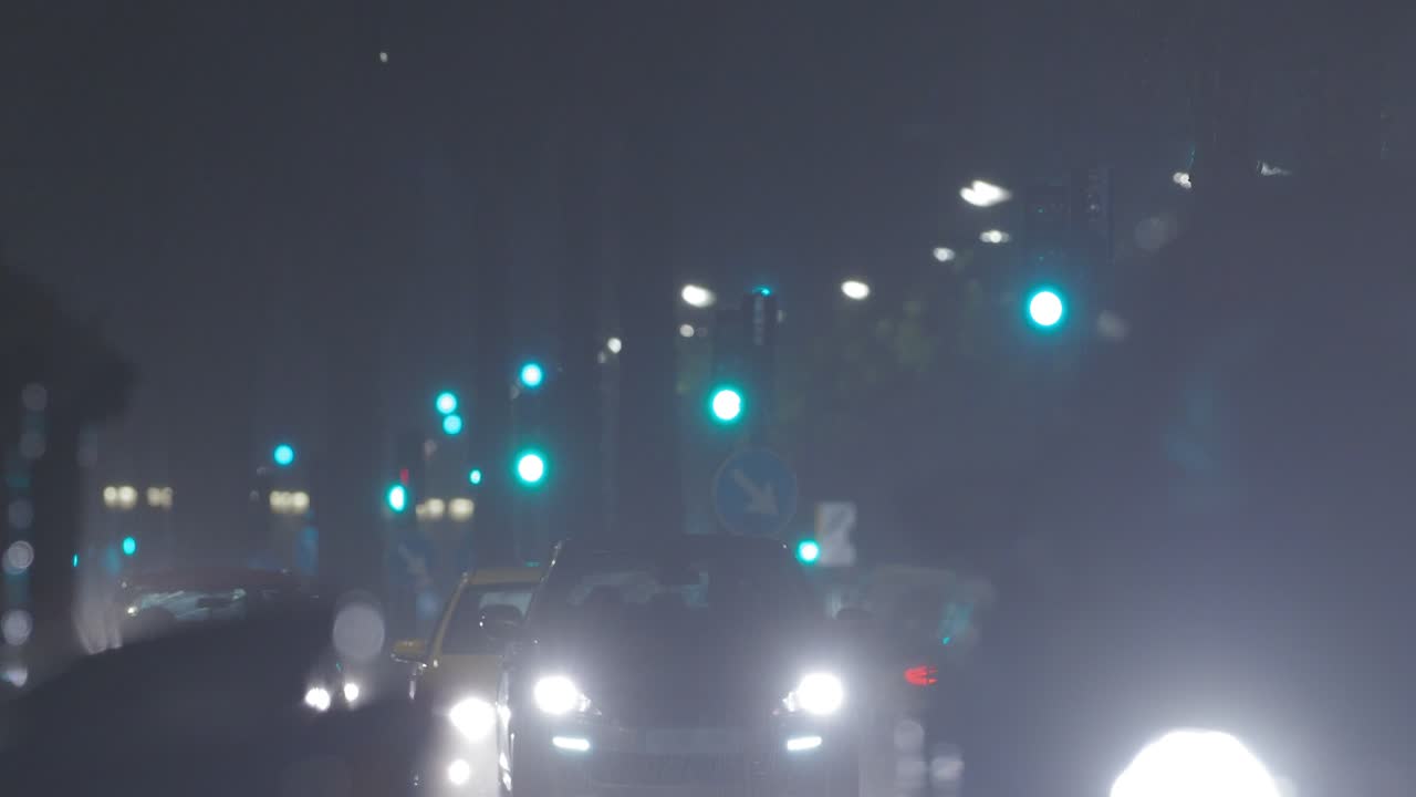 el resplandor cegador de los faros de los coches en movimiento bajo la lluvia por la noche